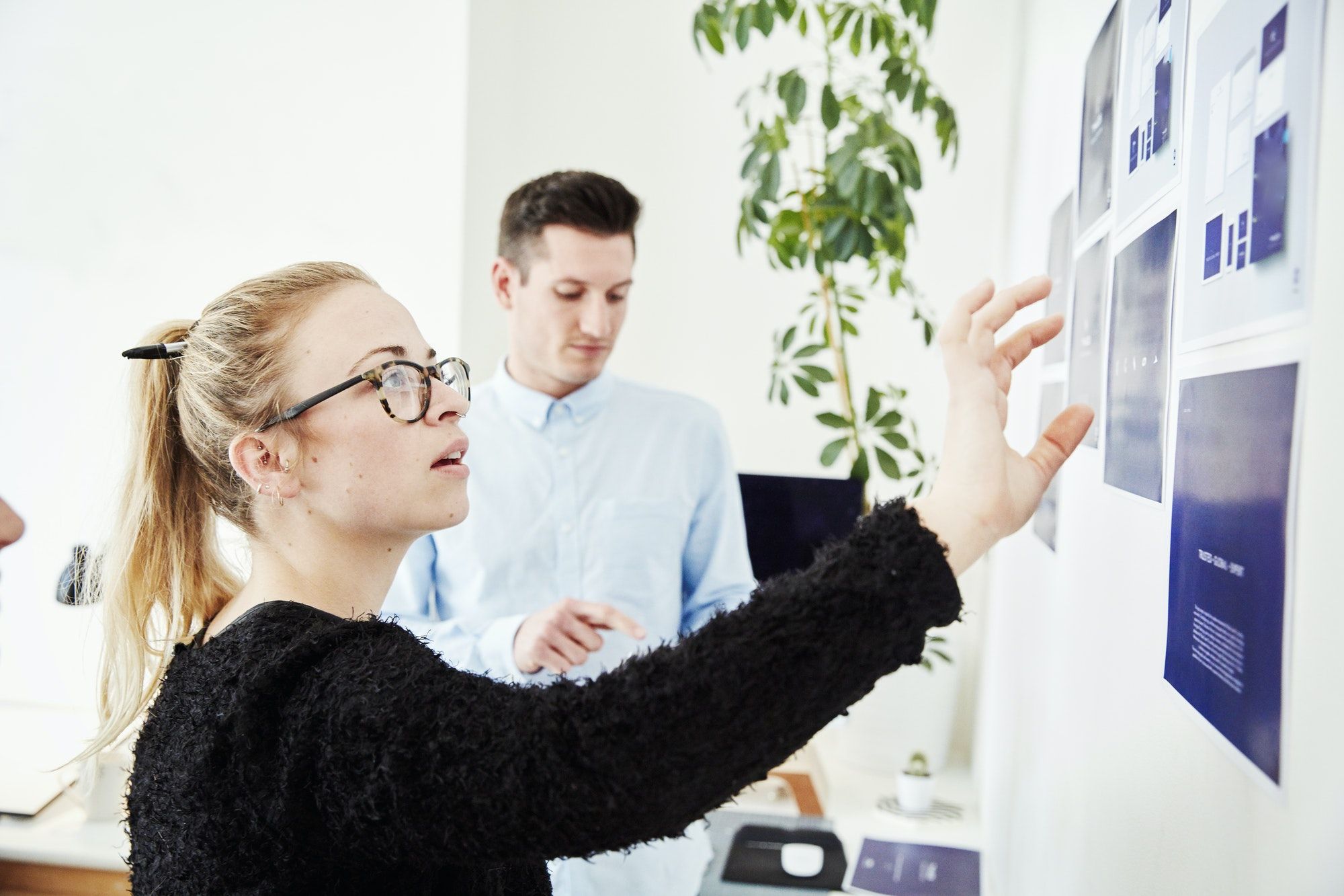 Two people looking at printed plans stuck on a wall, project management and discussions.